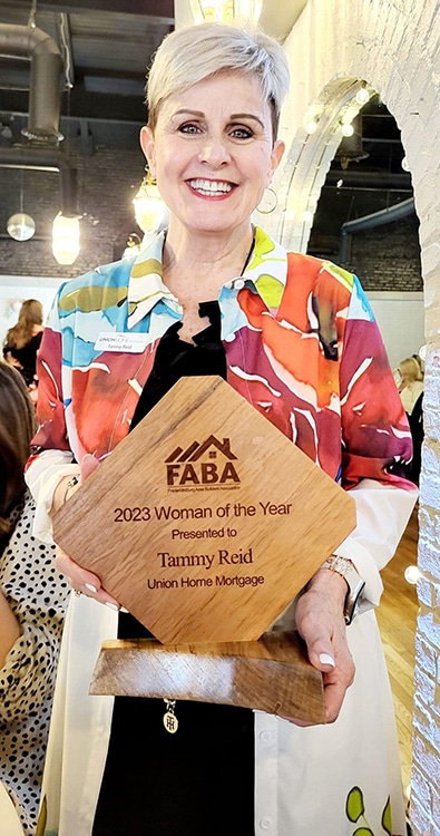 The image shows Tammy Reid holding a wooden plaque awarded by the Fredericksburg Area Builders Association (FABA), recognizing her as the 2023 "Woman of the Year." The plaque is inscribed with her name and her association with Union Home Mortgage. She is smiling in a celebratory setting, suggesting the award was presented at an event.