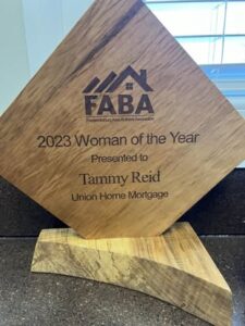 The image shows a wooden plaque awarded by the Fredericksburg Area Builders Association (FABA), recognizing Tammy Reid as the 2023 "Woman of the Year." The plaque is inscribed with her name and her association with Union Home Mortgage.